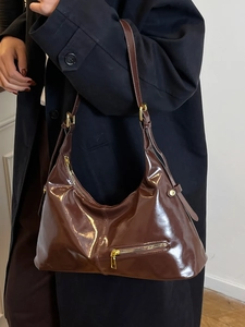 Sac hobo marron foncé brillant avec fermeture éclair dorée porté par un mannequin