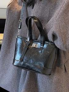 Sac seau chic en cuir brillant noir avec boucle argentée porté sur un manteau gris