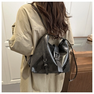 Detail of a vintage black leather backpack with metal buckles on a trench coat model