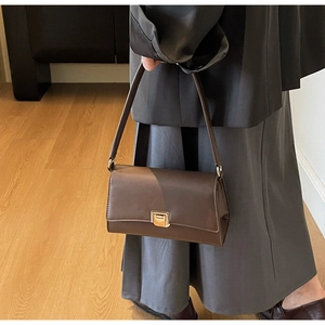 Detail of a brown leather baguette bag with golden square buckle on a model shoulder