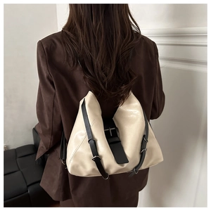 Rear view of a model wearing a minimalist beige glossy leather backpack with black straps