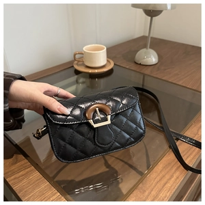 Detail shot of black quilted leather crossbody bag with vintage clasp on wooden table