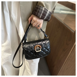 Close-up of black quilted leather crossbody bag featuring a gold buckle with wood grain