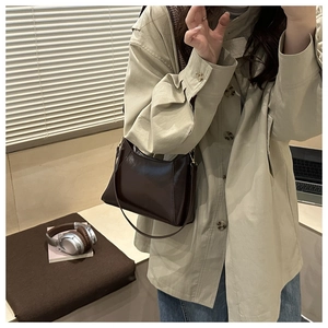 Détail d'un sac bandoulière en cuir café foncé au fini brillant et design trapèze minimaliste