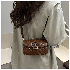 Detail of dark brown quilted small square bag worn on shoulder by model in studio
