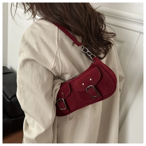 Detail of dark red suede shoulder bag with dual front pockets and silver buckles