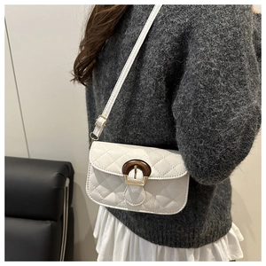 Detailed view of white quilted crossbody bag featuring gold hardware and brown ring clasp