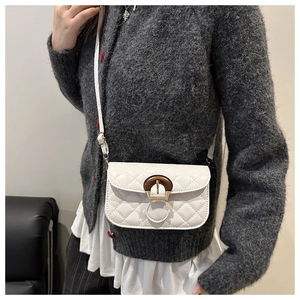 Close-up of white quilted crossbody bag with tortoiseshell buckle on a model's shoulder
