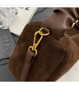 Gros plan sur les ferrures dorées et la poignée plissée d'un sac en daim marron