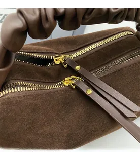 Détail du sac en daim marron foncé avec double fermeture éclair dorée et poignée plissée