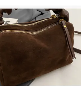 Détail d'un sac à main en daim marron foncé avec double fermeture et poignée plissée