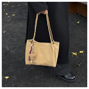 Detail of khaki tote bag with woven straps, bear charm, and matte texture on a black coat