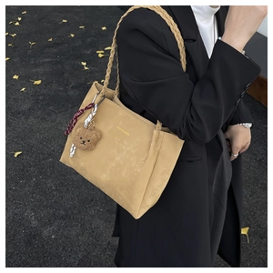 Detail of khaki suede tote bag with woven handles and a cute plush bear charm on the side