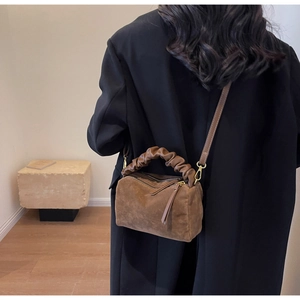 Sac oreiller en daim marron porté avec un manteau noir dans un décor minimaliste