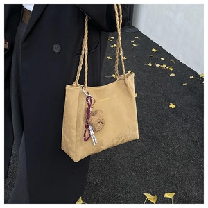 Detail of camel tote bag with woven handles, gold logo, and decorative bear pendant