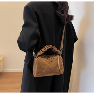 Détail d'un sac bandoulière en daim marron avec poignée plissée et boucle dorée