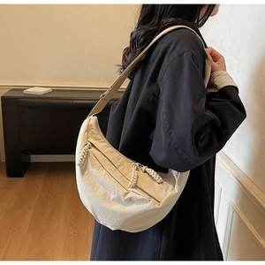 Detail of beige nylon crescent bag featuring chunky woven rope zipper and adjustable strap