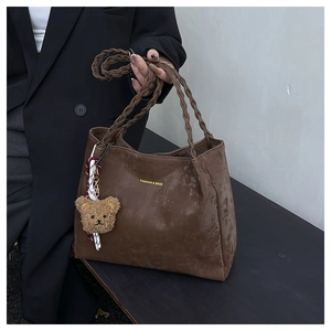 Detail of brown matte tote bag with woven handles and cute teddy bear charm