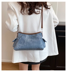 Detail of blue denim shoulder bag with brown leather trim and silver metal hardware