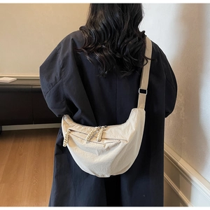 Detail of a beige crescent crossbody bag showing its nylon texture and adjustable strap