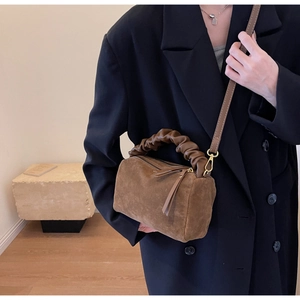 Sac bandoulière en daim marron avec poignée froncée porté par un mannequin