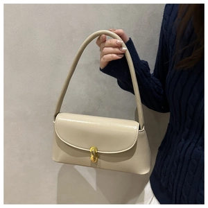 Detail of beige leather shoulder bag with gold metal buckle held by a model