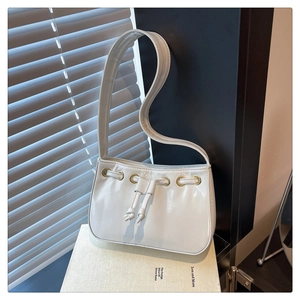 Close-up of cream glossy shoulder bag with gold eyelets on art book with soft shadows