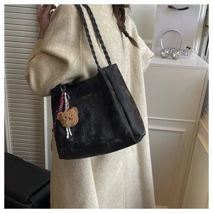 Close-up of black tote bag with retro matte texture, gold lettering and plush bear charm