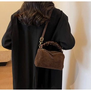 Détail du sac en daim marron avec poignée plissée, pompons et bandoulière amovible réglable
