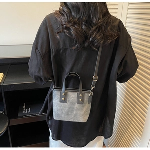 Modern grey matte crossbody bucket bag shown with dual handles and gold studs on a model