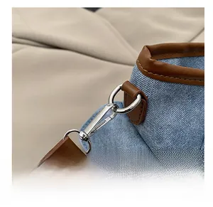 Detailed view of silver lobster clasp on blue denim shoulder bag with brown leather trim