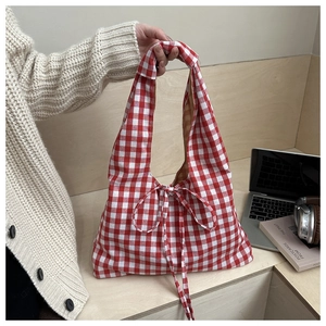 Detail of red gingham tote bag featuring a decorative bow on light wood background