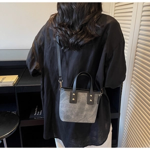 Detail of grey frosted tote bag with black leather handles and gold stud accents
