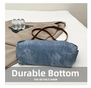 Detail view of the durable bottom of this blue denim shoulder bag with leather strap
