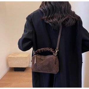 Détail d'un sac oreiller en daim marron avec anse à volants et boucle en métal doré