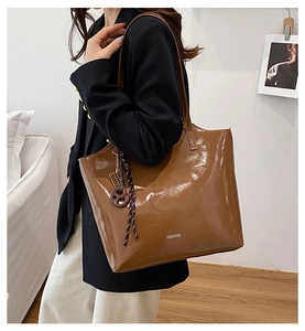 Detail of glossy brown tote bag with white FASHION text and woven charm accessory