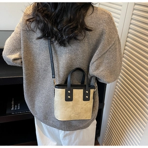 Back view of model wearing a mini beige bucket bag with black leather straps and rivets