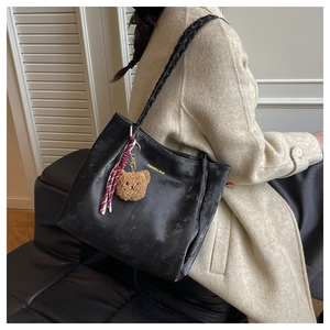 Close-up of black tote bag featuring a woven shoulder strap and cute teddy bear charm