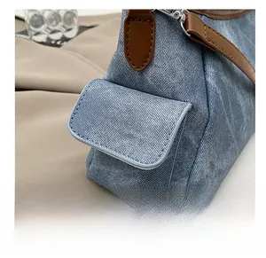 Detail of blue denim shoulder bag showing side flap pocket and brown leather trim accents