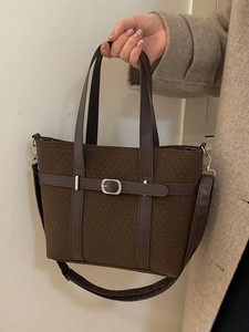 Brown woven tote bag with V-pattern and metal buckle held by model in beige coat