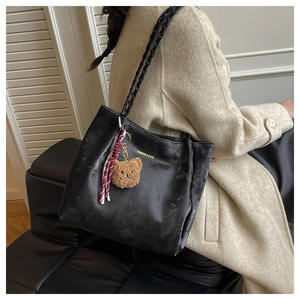 Detail of black leather tote bag with braided handle and cute brown plush bear charm