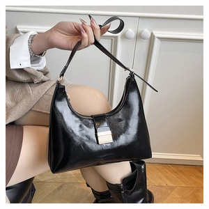 Detail of glossy black leather hobo bag with gold metal buckle and adjustable strap