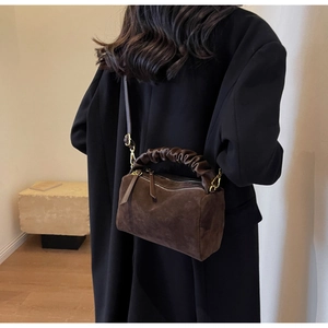 Détail d'un sac à bandoulière en daim marron avec poignée plissée sur manteau noir