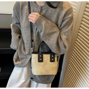 Detail of a beige suede crossbody bucket bag with black handles on a casual outfit