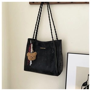 Detail of black tote bag with gold lettering, woven straps, and brown bear pendant