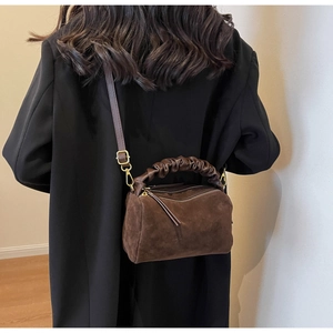 Détail du sac en daim marron foncé avec poignée plissée porté sur un manteau noir