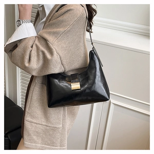Close-up of black glossy chain bucket bag with golden metal clasp on a model