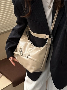 Sac hobo demi-lune beige avec boucle métallique porté par un mannequin en costume rayé
