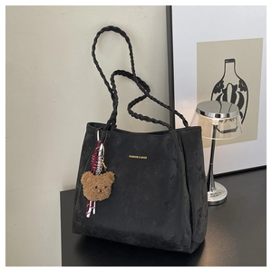 Detail of black suede tote bag with woven shoulder strap and brown plush bear charm