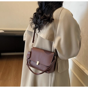Détail d'un sac bandoulière marron avec boucle dorée sur un trench-coat beige